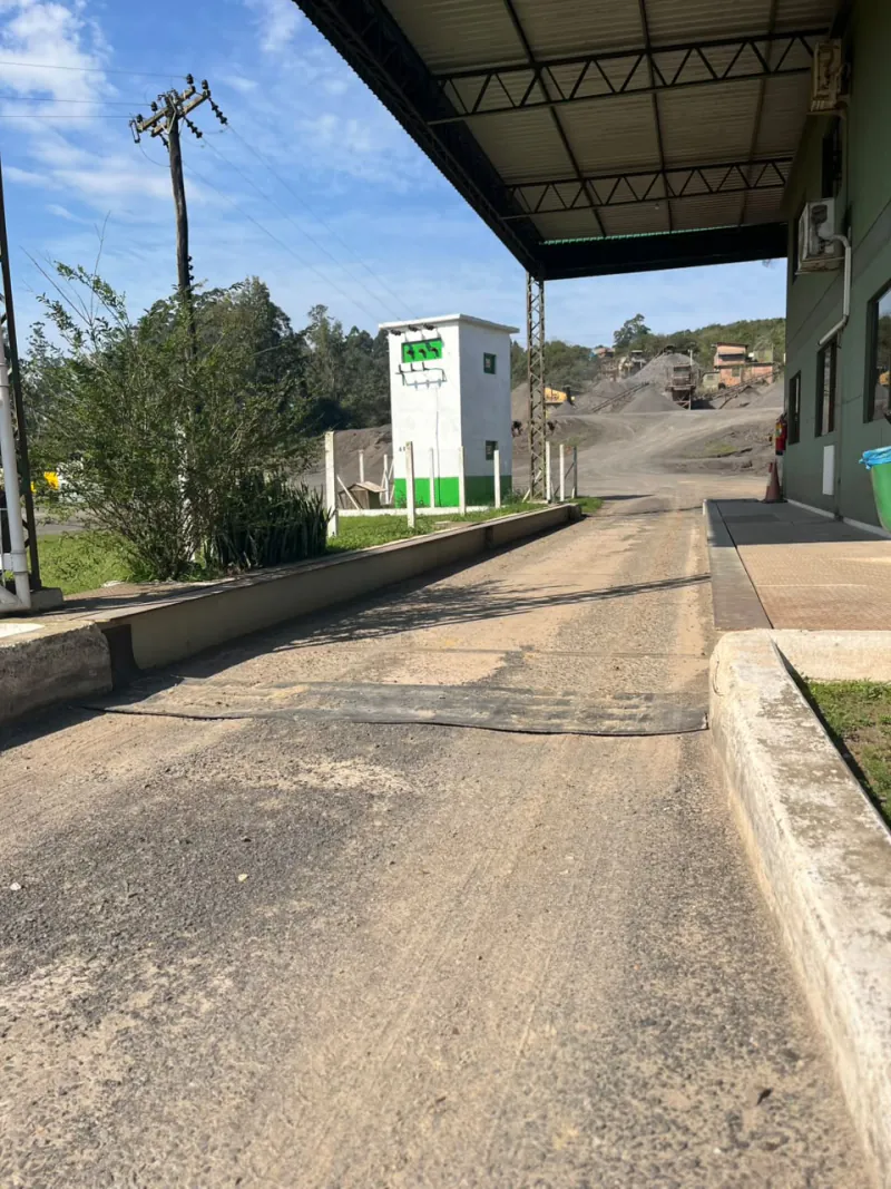 Balança de caminhões na expedição, com a planta de britagem ao fundo